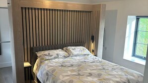 Een moderne slaapkamer met een bed, nachtkastje, stoel en raam.