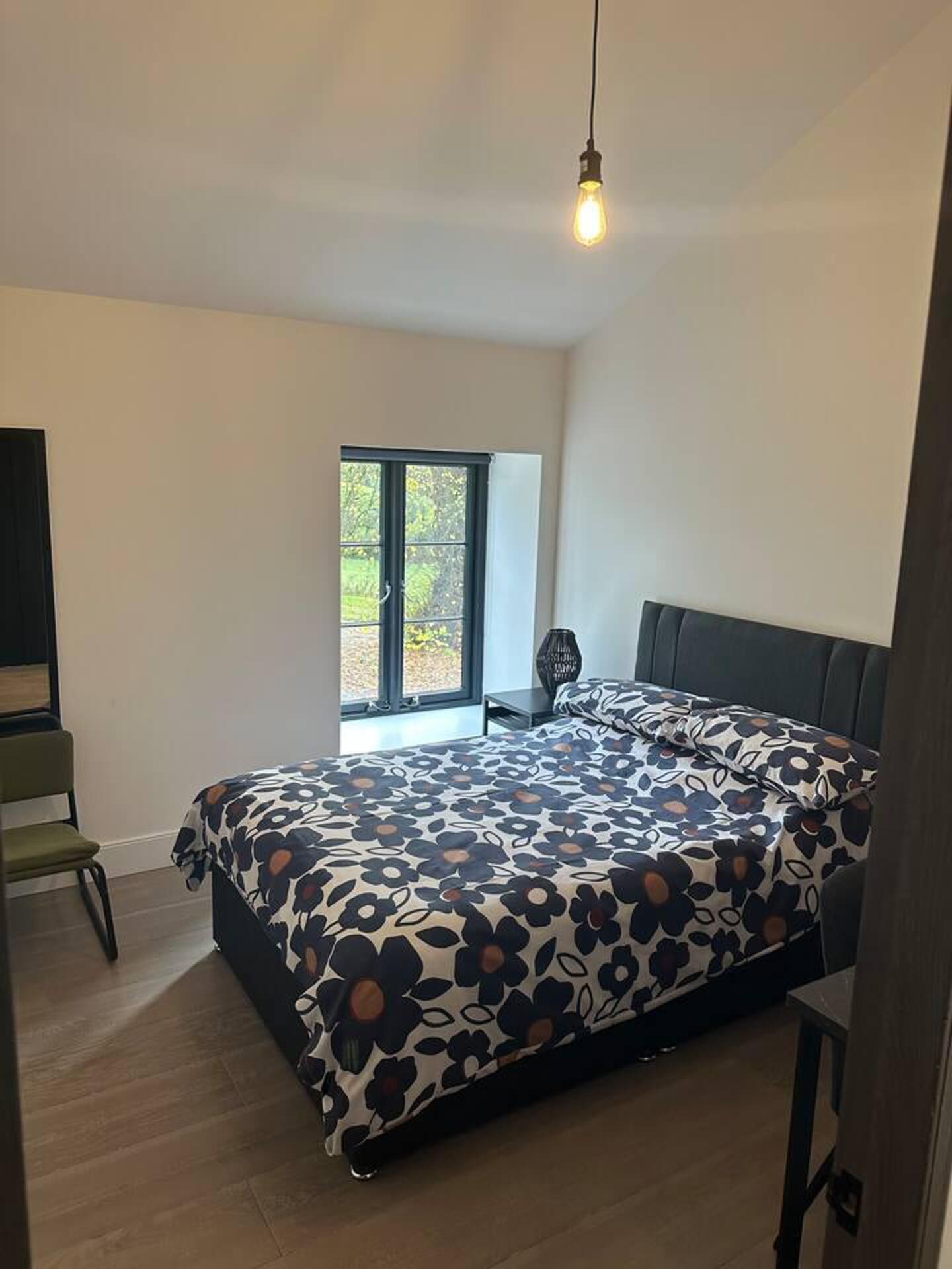 A modern bedroom with a large bed, a window, and a hanging light fixture.
