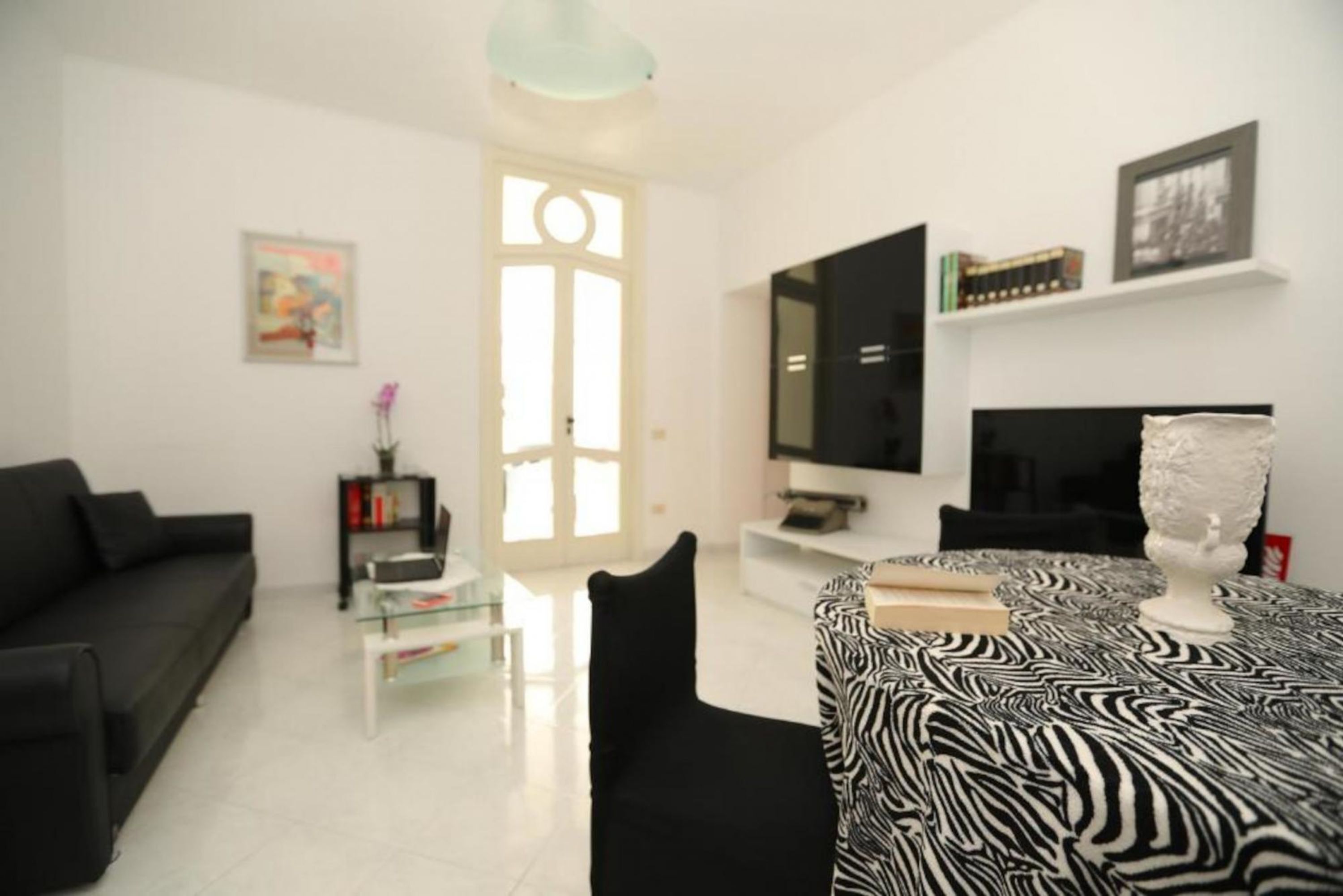 A modern living room with a black sofa, a glass coffee table, a zebra-patterned table, a flat-screen TV, and a fireplace.