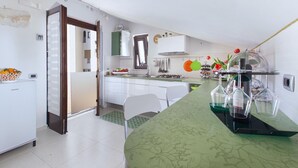 Una cocina moderna con armarios blancos, encimera verde y zona de comedor con mesa y sillas blancas.