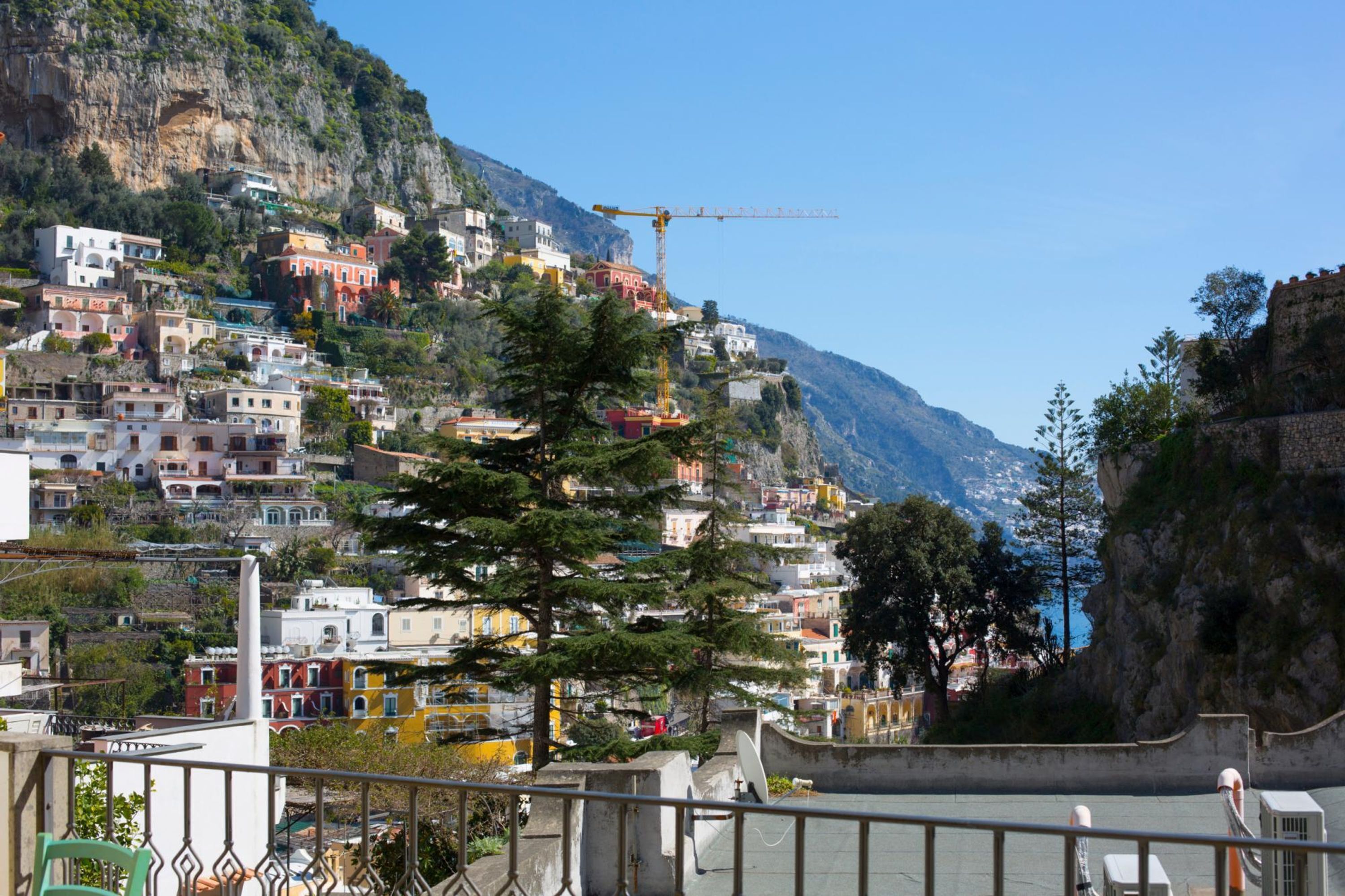 Une ville côtière aux bâtiments aux couleurs vives, avec une grue de construction et un paysage montagneux en arrière-plan.