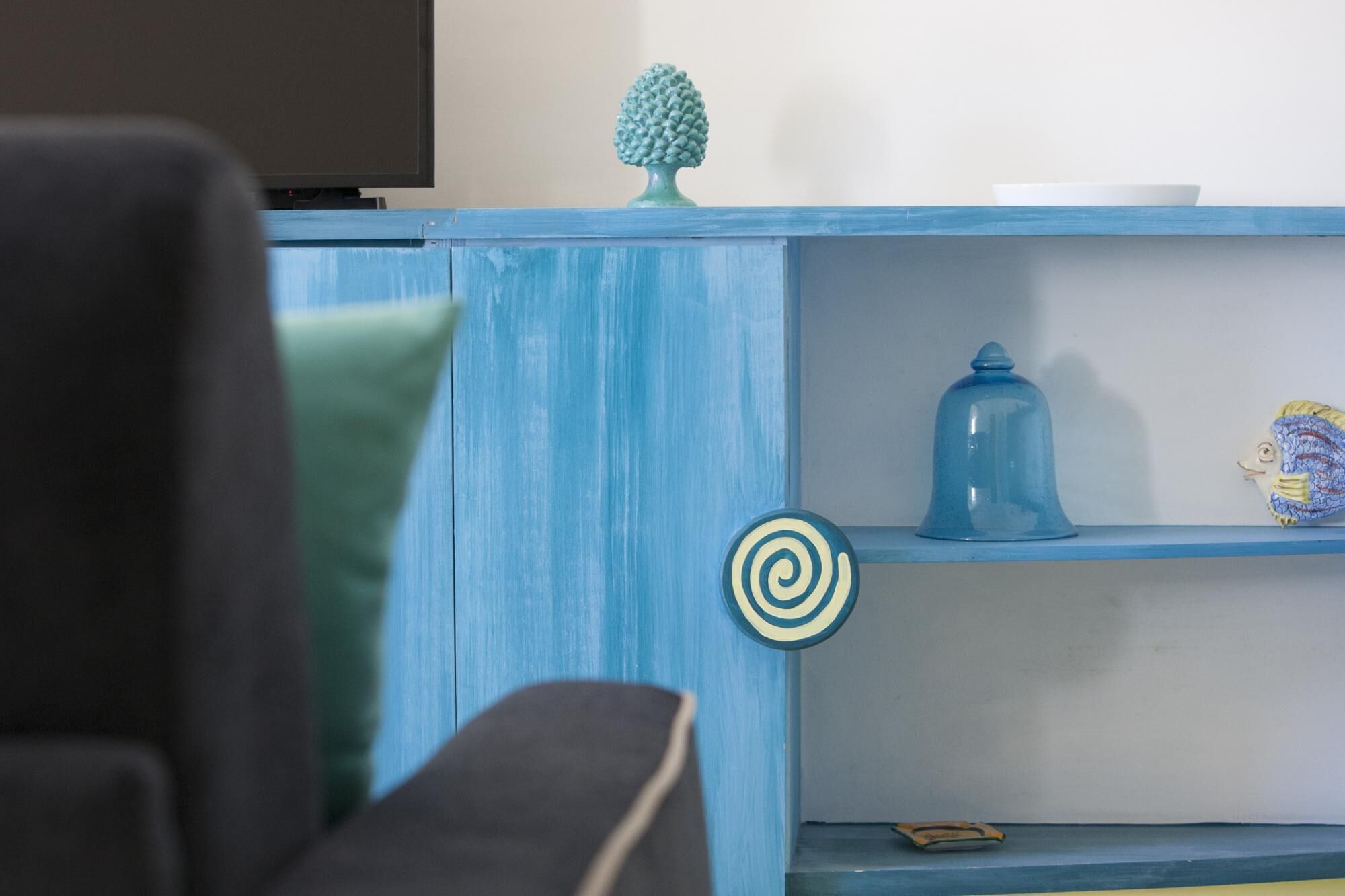 A blue painted cabinet with shelves, a decorative pineapple, and a bell.