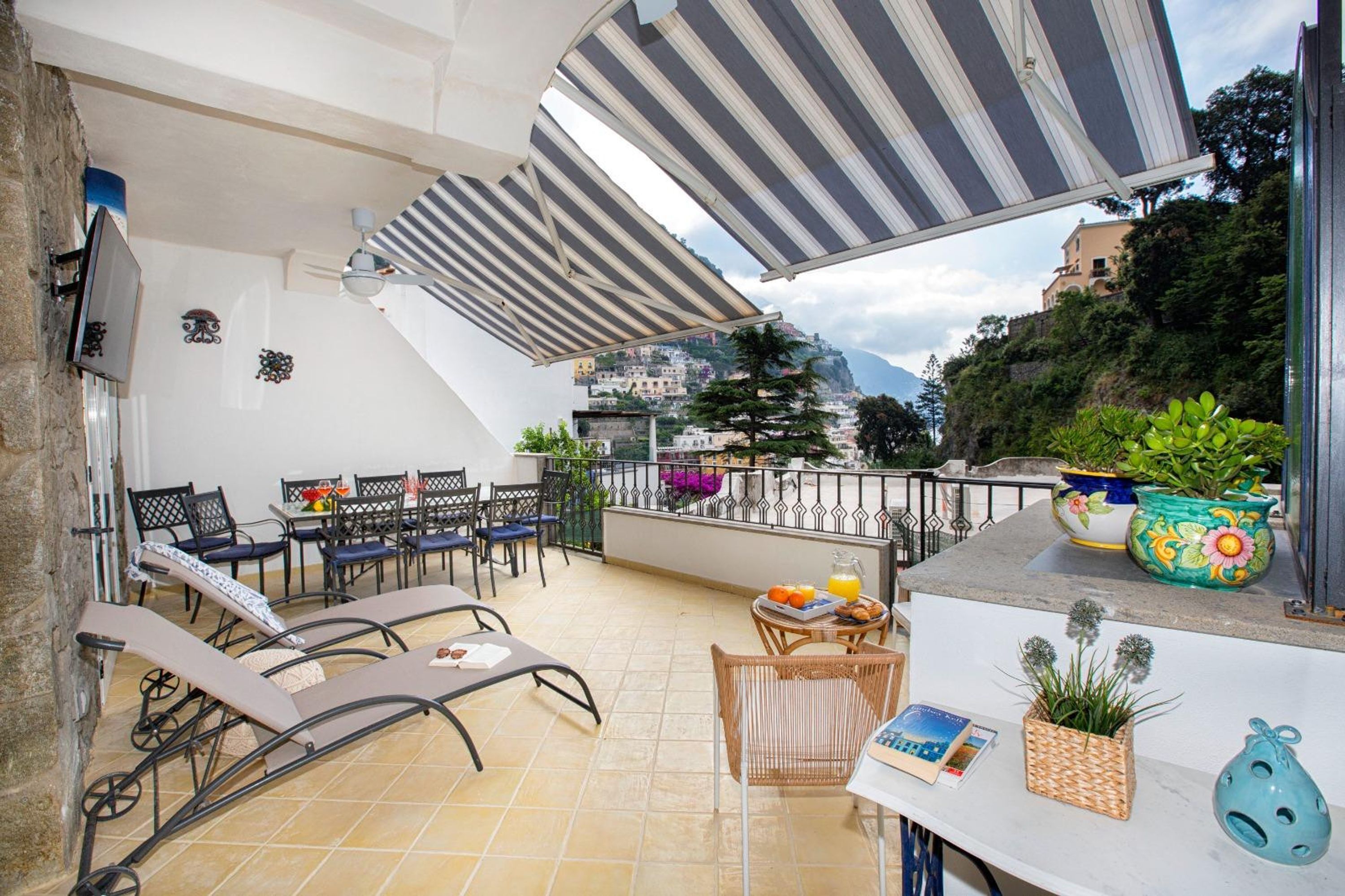 A terrace with sun loungers, a table with breakfast, and a view of a hillside town.