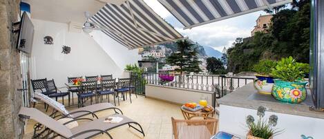 A terrace with sun loungers, a table with breakfast, and a view of a hillside town.