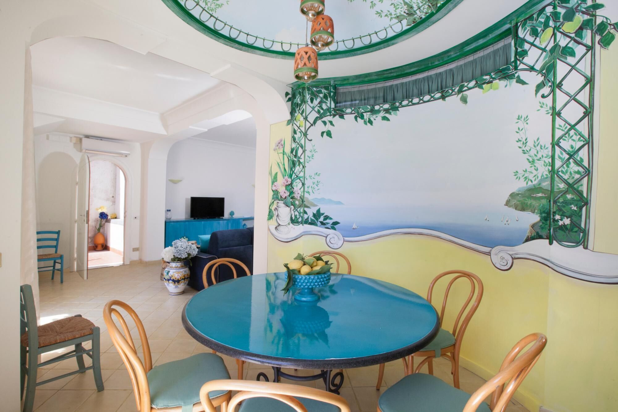 A dining area with a round table, chairs, and a mural of a coastal scene.