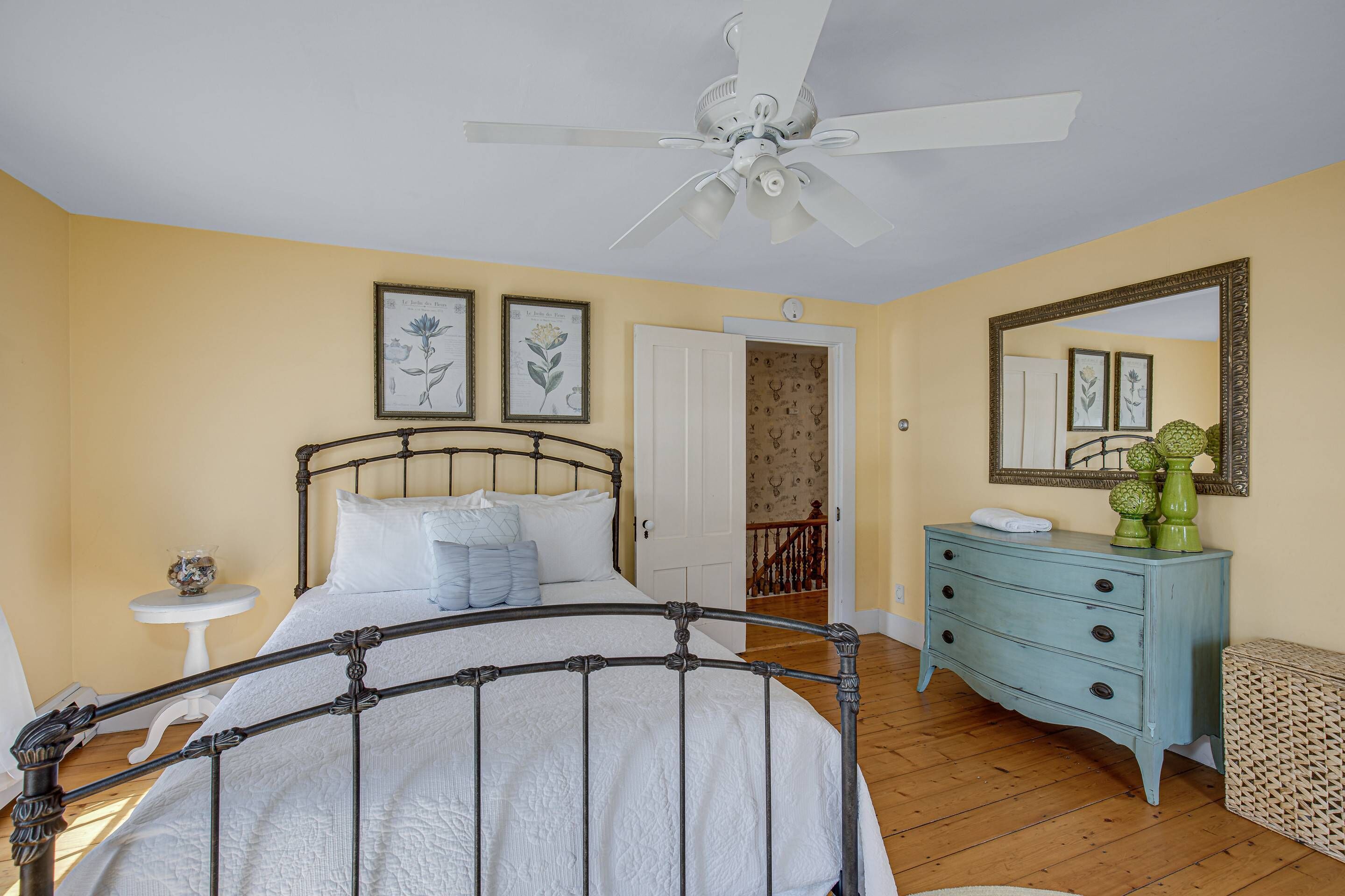A bedroom with a bed, a dresser, a mirror, and a ceiling fan.