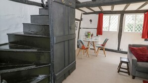 A staircase leading to a dining area with a table and chairs, a grey sofa, and a red curtain. - Bluebell Cottage (Stratford-upon-Avon)