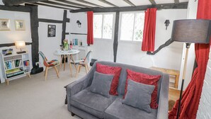 A cozy room with a grey sofa, red cushions, a small dining table, and a bookshelf. - Bluebell Cottage (Stratford-upon-Avon)