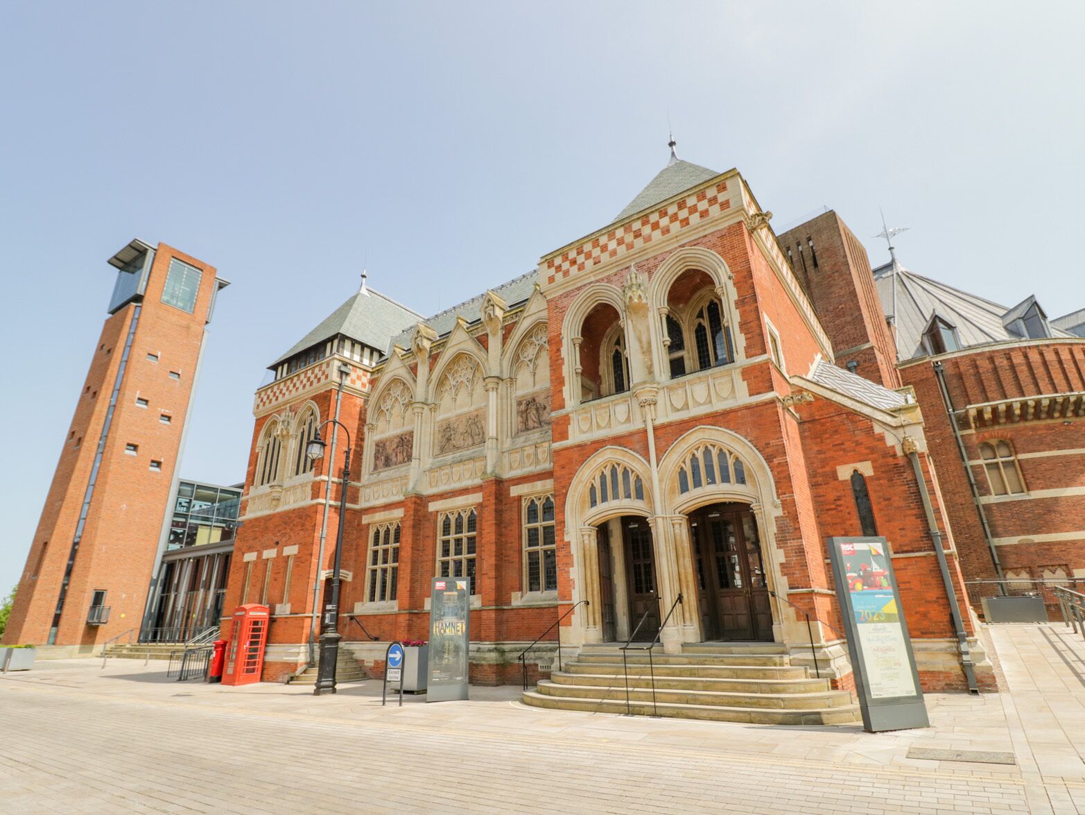A historic building with a prominent arched entrance, a clock tower, and a red telephone booth.