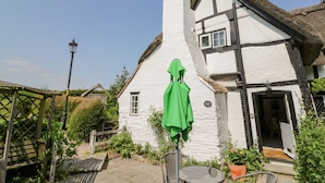 A traditional white house with a thatched roof, a green umbrella, and a wooden bench in the garden. - Bluebell Cottage (Stratford-upon-Avon)