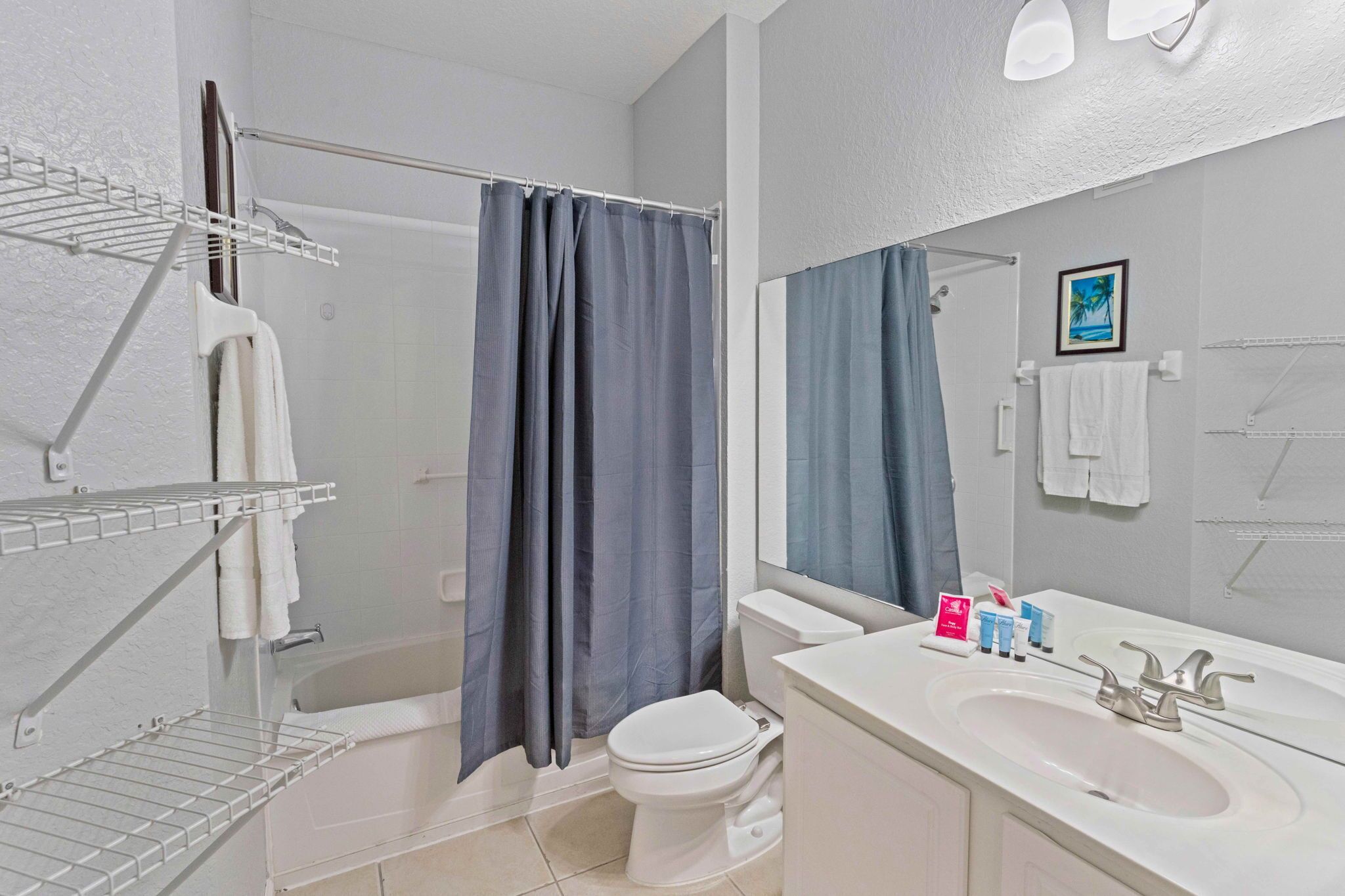 A bathroom with a bathtub, toilet, and sink. There are shelves with towels and toiletries.