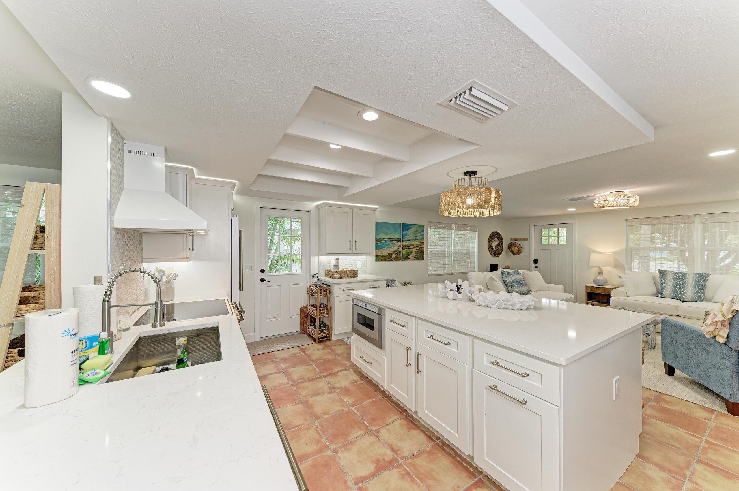A modern kitchen with white cabinetry, a large island, and a dining area with a blue sofa.