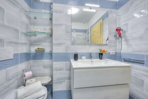 A bathroom with a white sink, a mirror, and a glass shelf with toiletries. - Marina's Green Home - Terrace and Parking (Riva del Garda)
