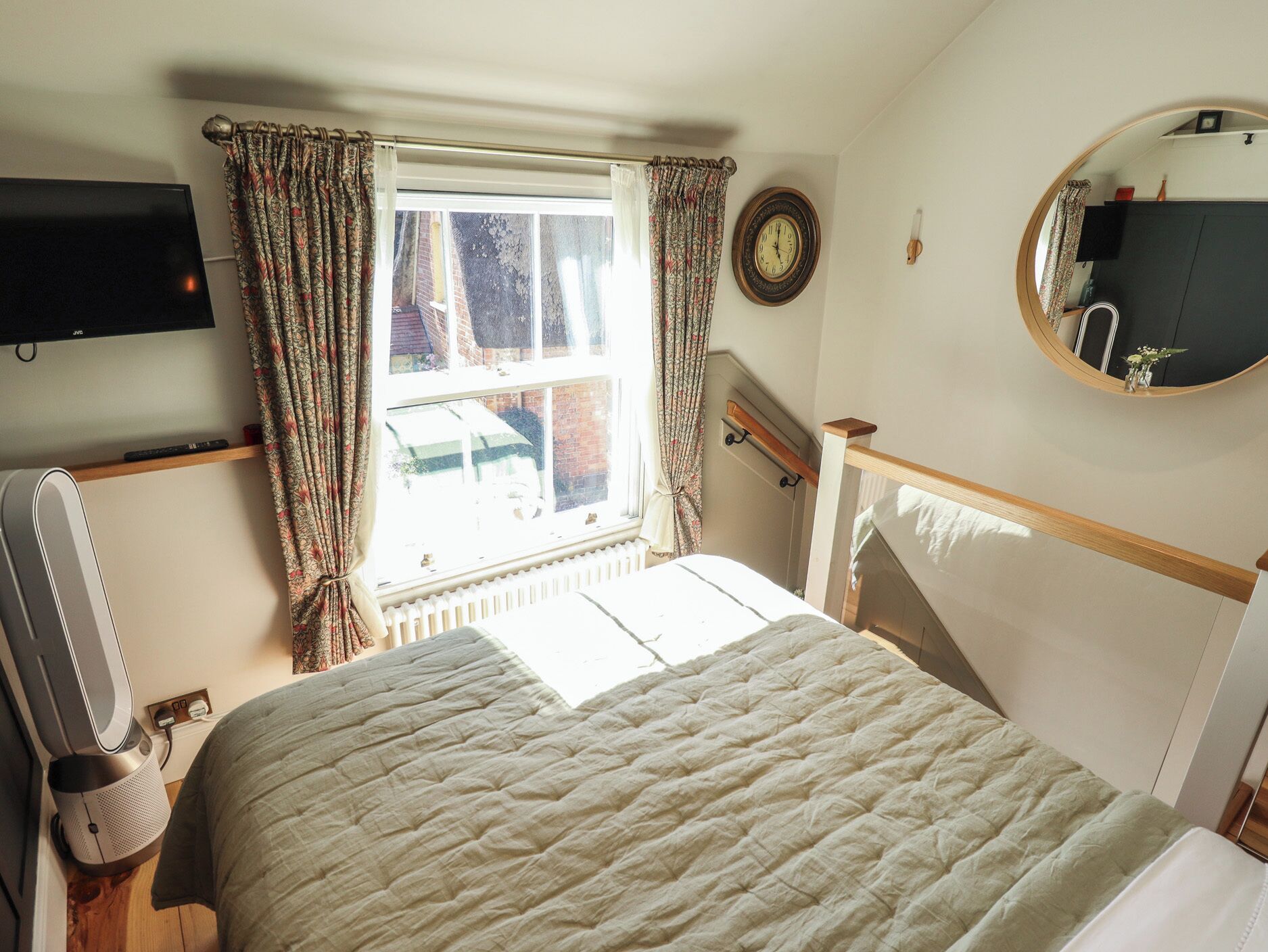 A bedroom with a bed, a TV, a clock, and a window with curtains.