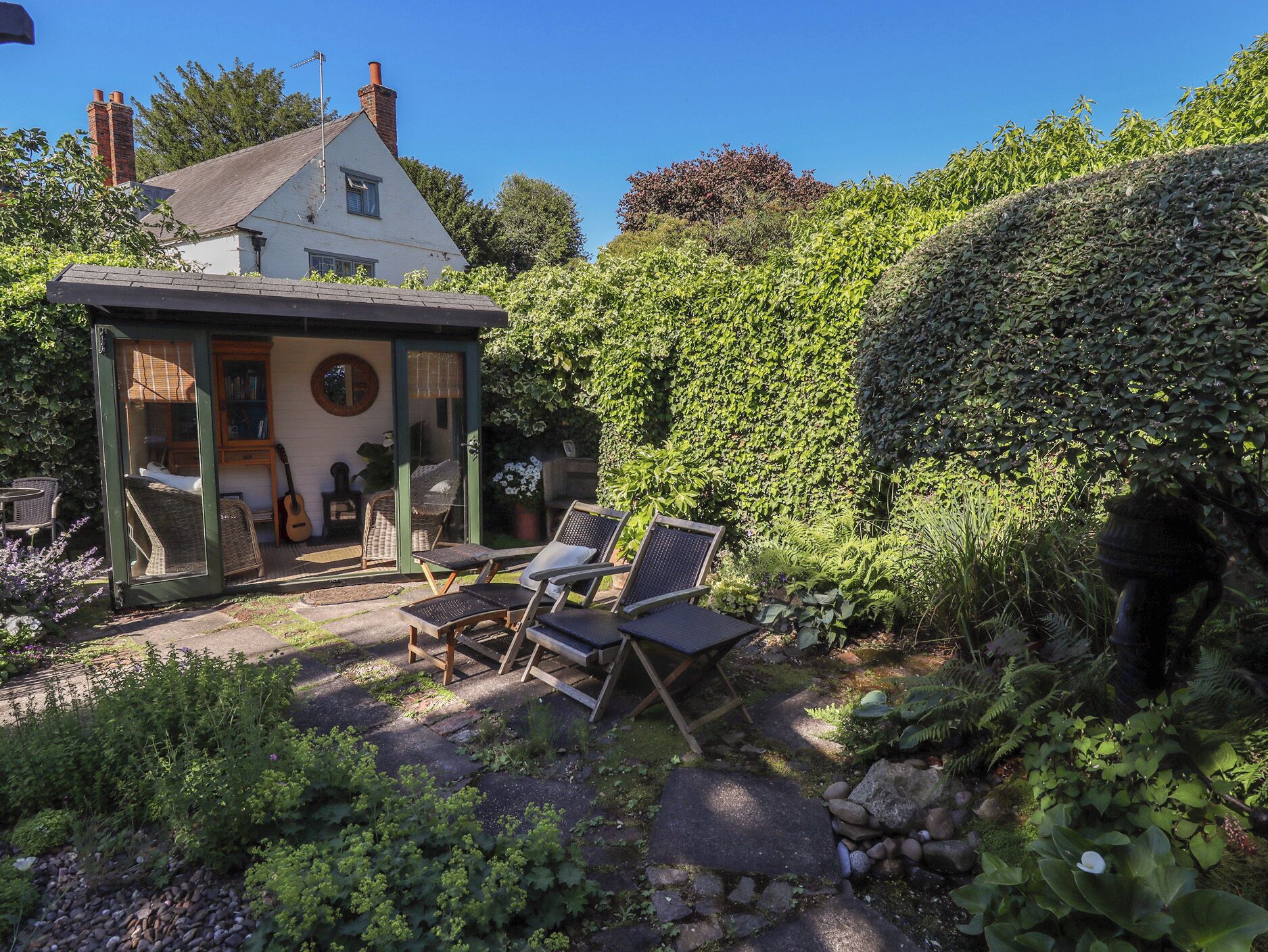 Une maison avec un patio et un coin salon extérieur, ainsi qu’une haie.
