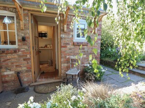 Una casa de ladrillo con puerta de madera, un pequeño espacio para sentarse al aire libre y un jardín con diversas plantas.