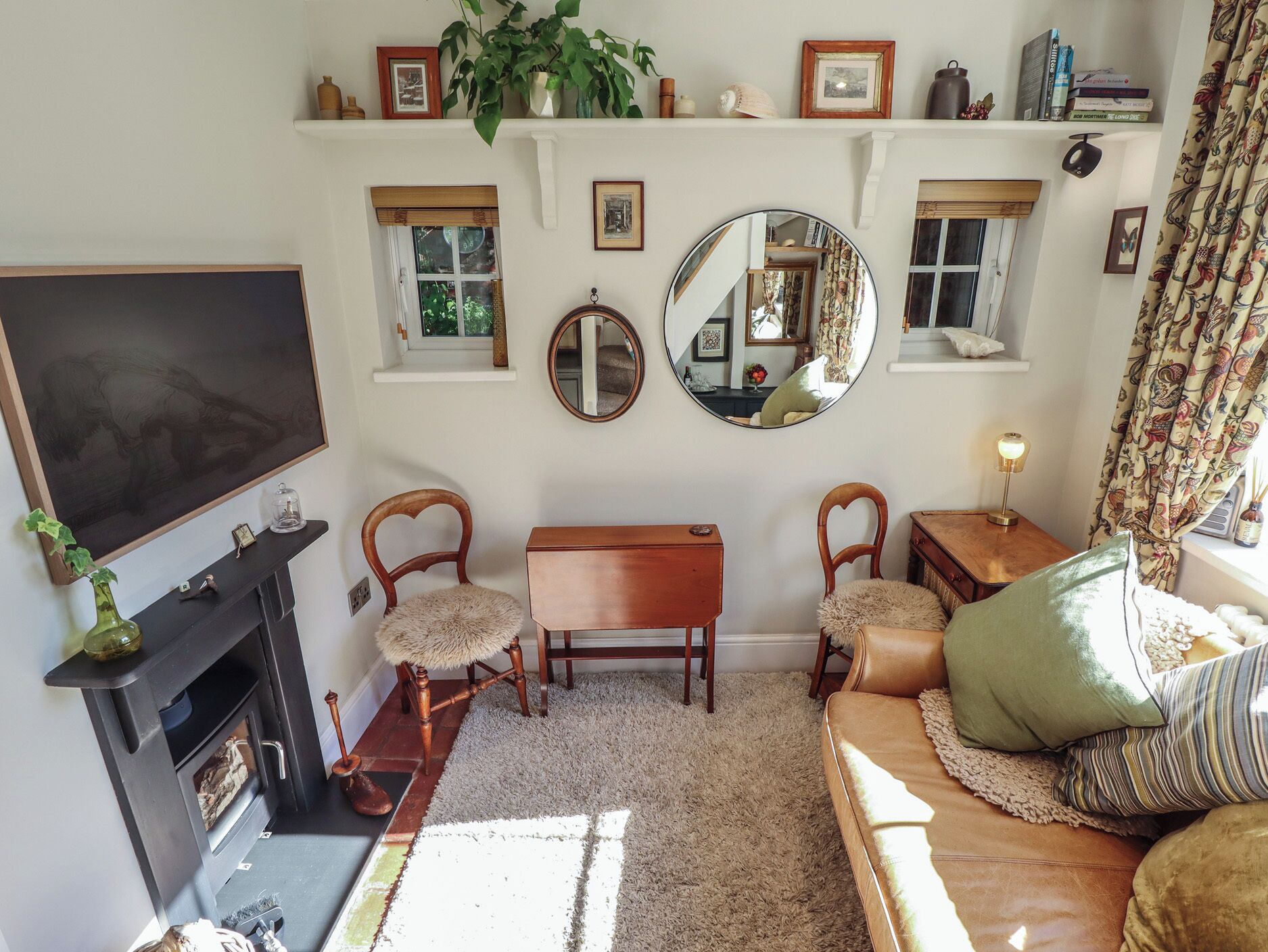 A living room with a fireplace, two wooden chairs, a sofa, a television, and a mirror.