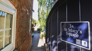 A narrow alleyway leading to a black gate with a sign reading '3a St Mary's Square' and social media icons. - Hangmans Cottage (Horncastle)