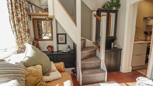 A living room with a sofa, a staircase, a kitchen area, and a dining table. - Hangmans Cottage (Horncastle)