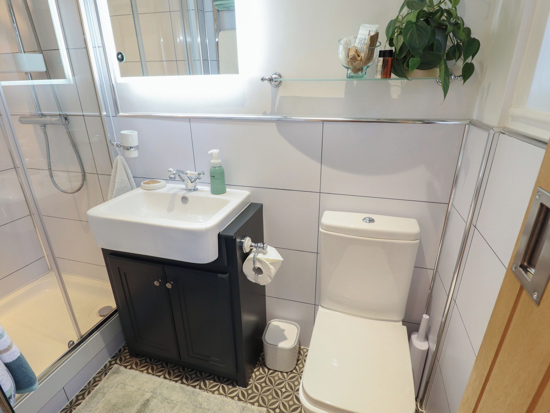 A bathroom with a shower, sink, toilet, and a small shelf with toiletries.
