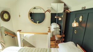 A bedroom with a bed, a round mirror, a wardrobe, a clock, and a staircase. - Hangmans Cottage (Horncastle)