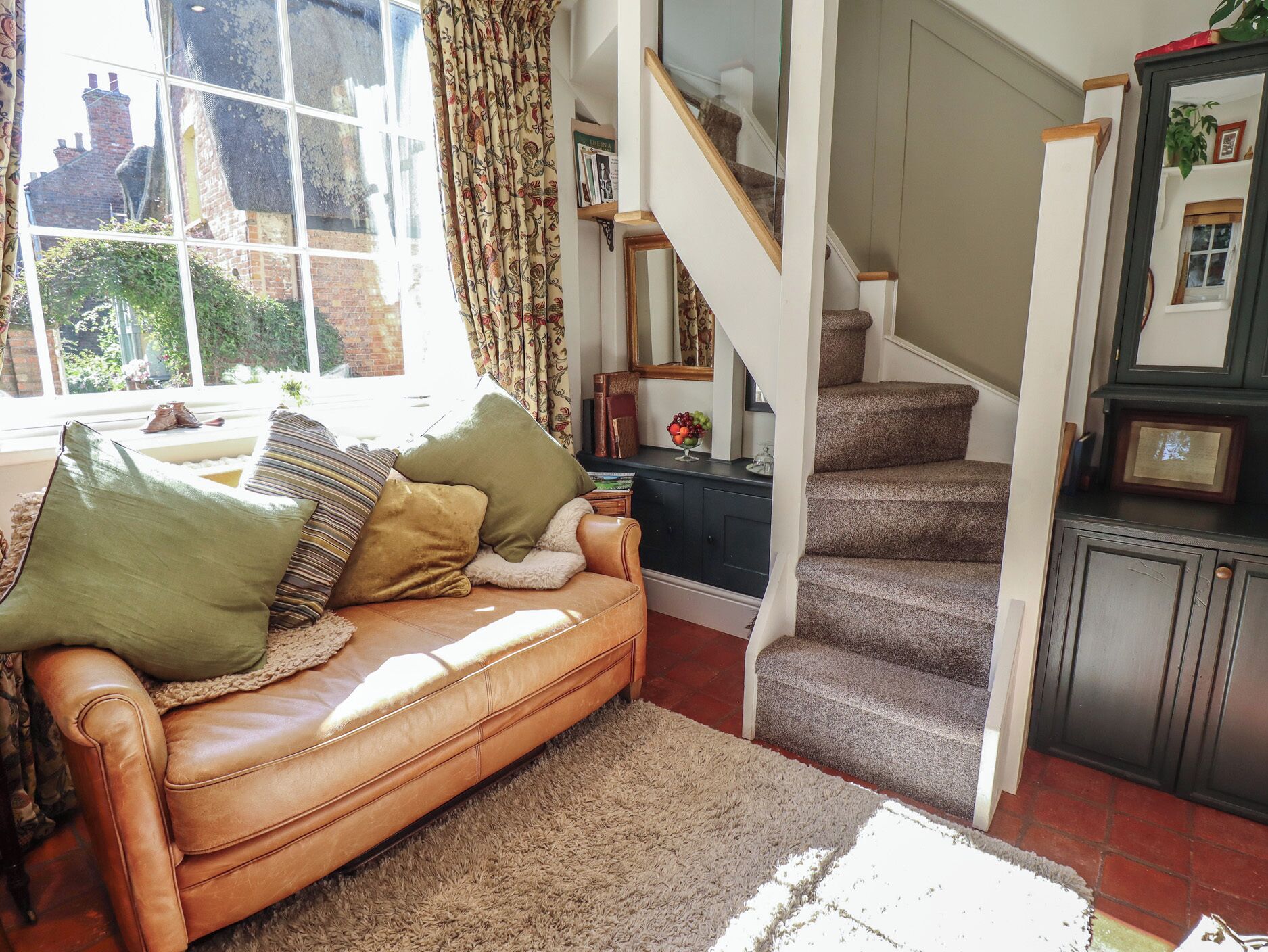 A living room with a leather sofa, a staircase, and a view of the outside.