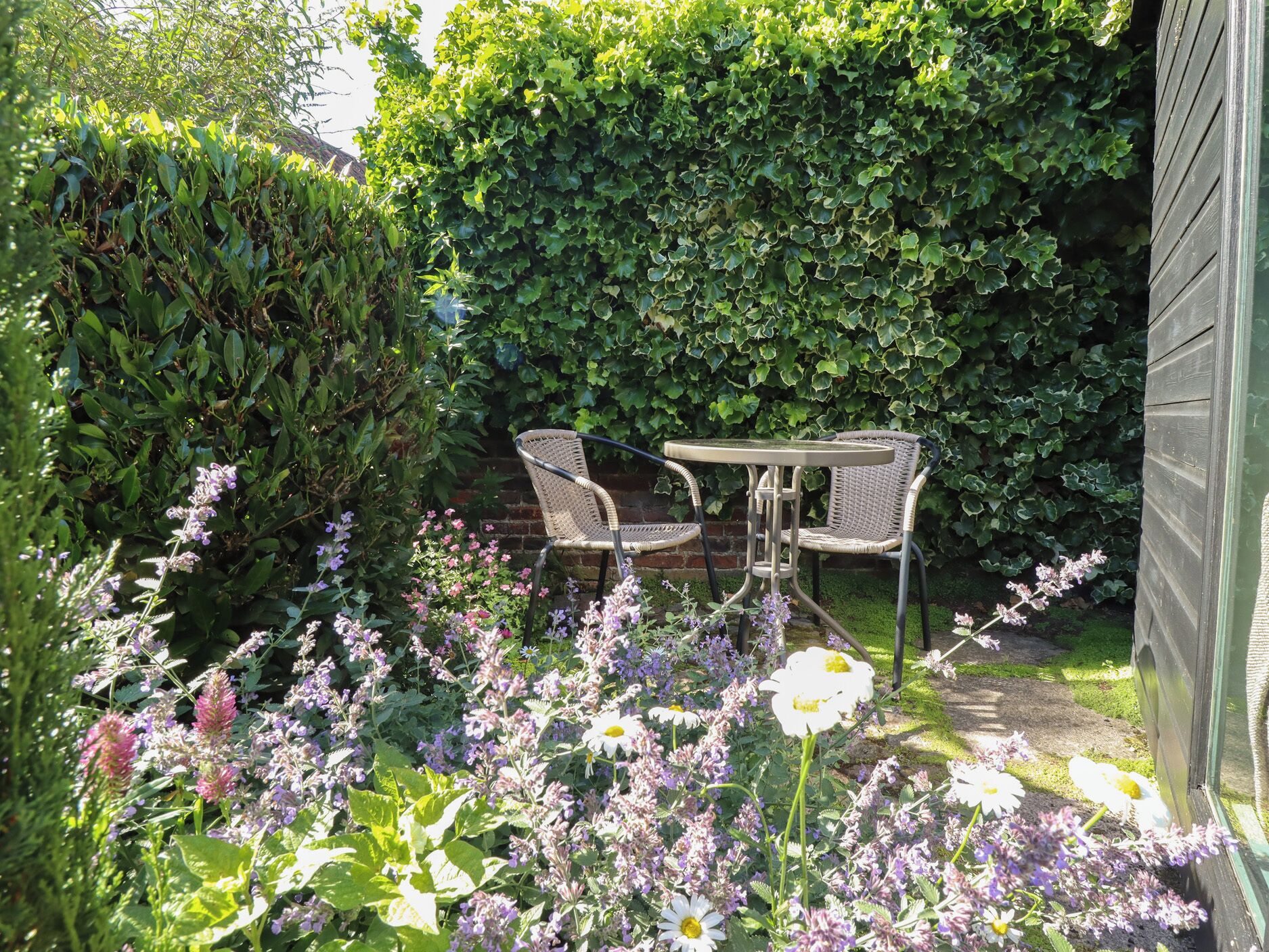 A garden with a table and chairs, surrounded by lush greenery and flowering plants.