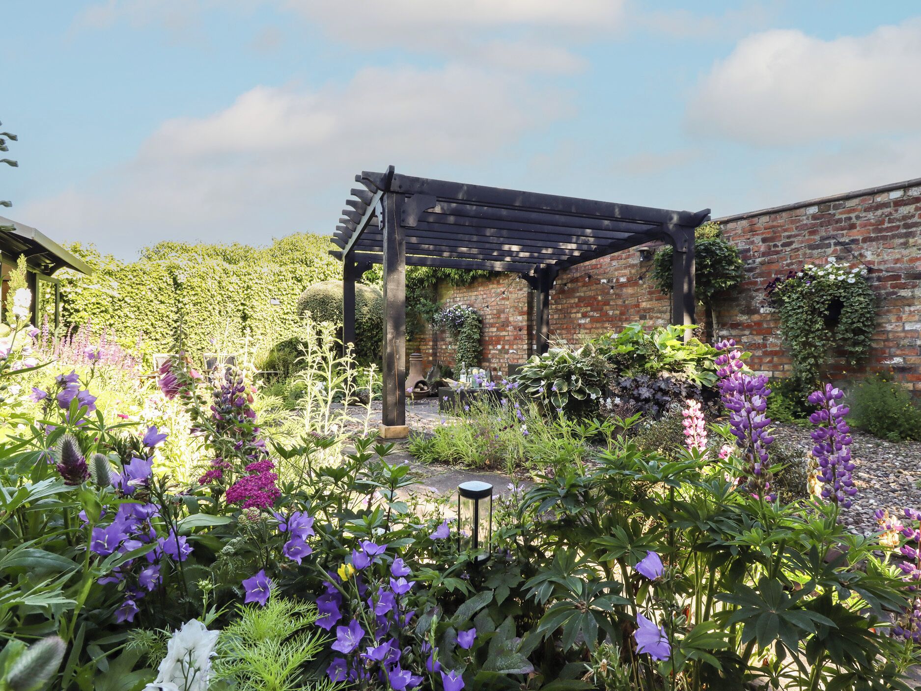 A garden with a pergola, brick wall, and various plants.