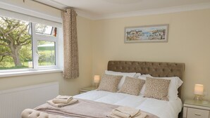 A neatly made bed with a tufted headboard, a window with a view of greenery, and a framed picture on the wall. - Erwlon (Aberystwyth)