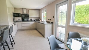 A modern kitchen with a dining area, featuring a glass table, bar stools, and a view through large windows. - Erwlon (Aberystwyth)