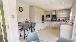 A modern kitchen with white cabinets, a dining area with two chairs, and a glass table with a vase of flowers. - Erwlon (Aberystwyth)