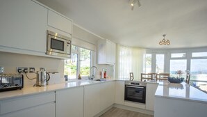 A modern kitchen with white cabinets, a built-in microwave, a toaster, and an oven. - E19 The Warren (Pwllheli)