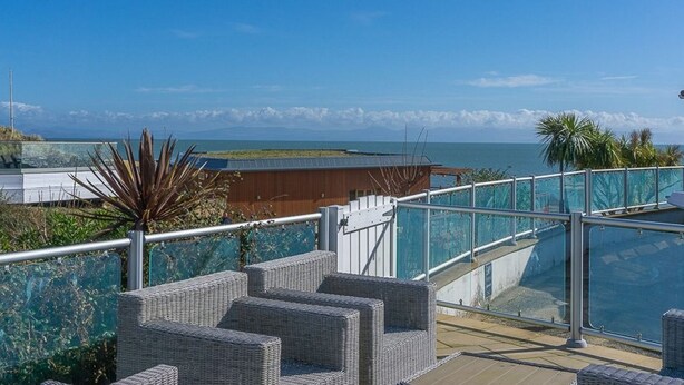 A balcony with wicker furniture overlooking a coastal view. - E19 The Warren (Pwllheli)