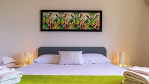 A neatly made bed with white linens, a green quilt, and a tropical floral artwork above it. - Villetta Mari e Amuri (Giardini Naxos)