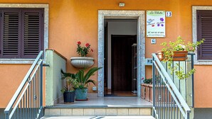 A building entrance with a staircase, potted plants, and a signboard. - Villetta Mari e Amuri (Giardini Naxos)