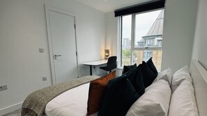 Une chambre moderne avec un grand lit, un bureau et une fenêtre donnant sur la ville.