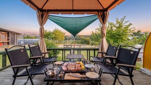 An outdoor patio with a table set for a barbecue, surrounded by chairs, under a canopy.