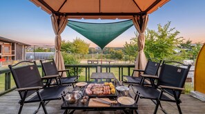 Une terrasse extérieure avec une table dressée pour un barbecue, entourée de chaises, et protégée par un auvent.