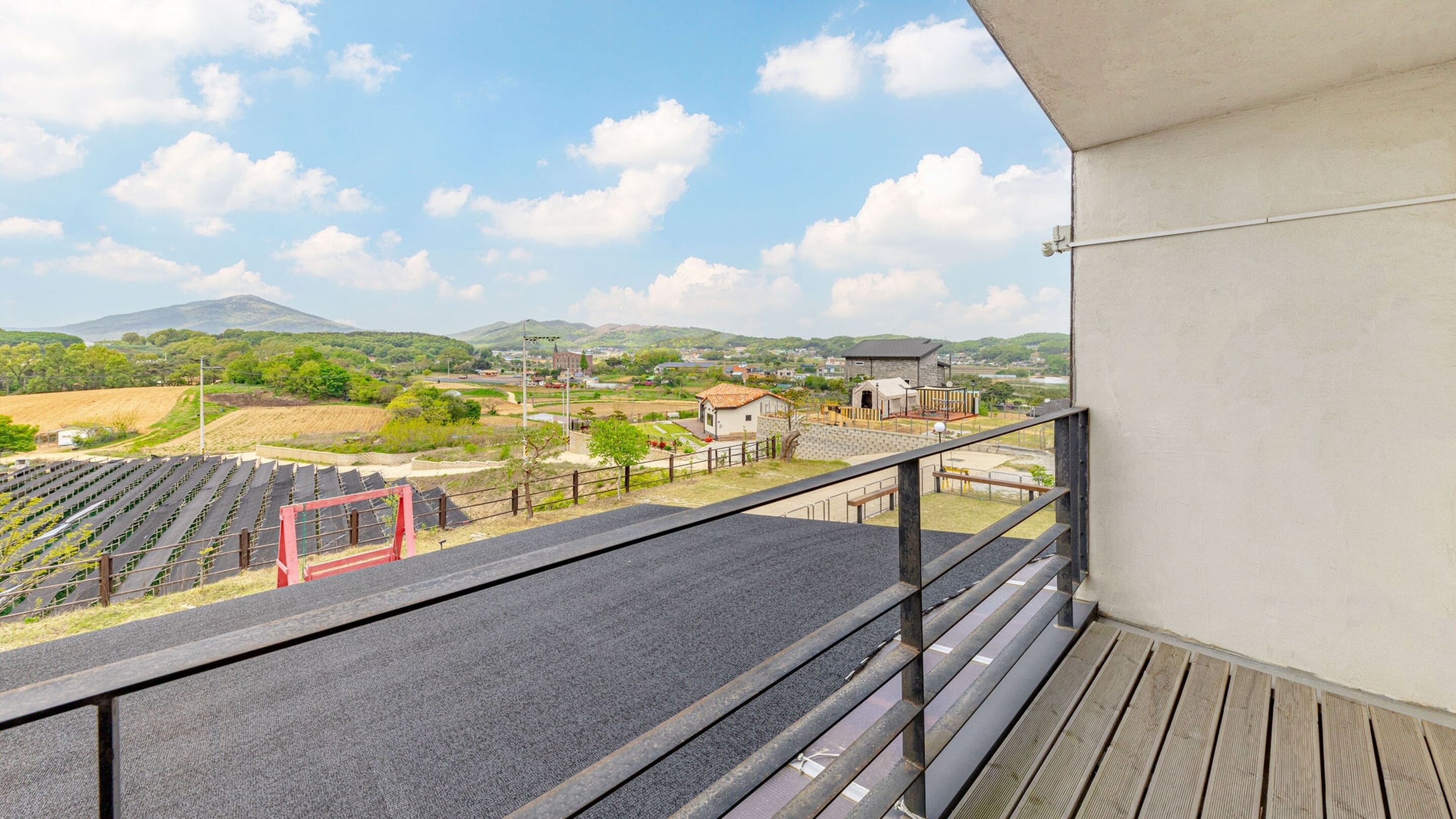 A balcony with a view of a vineyard, a small building, and a mountain in the distance.