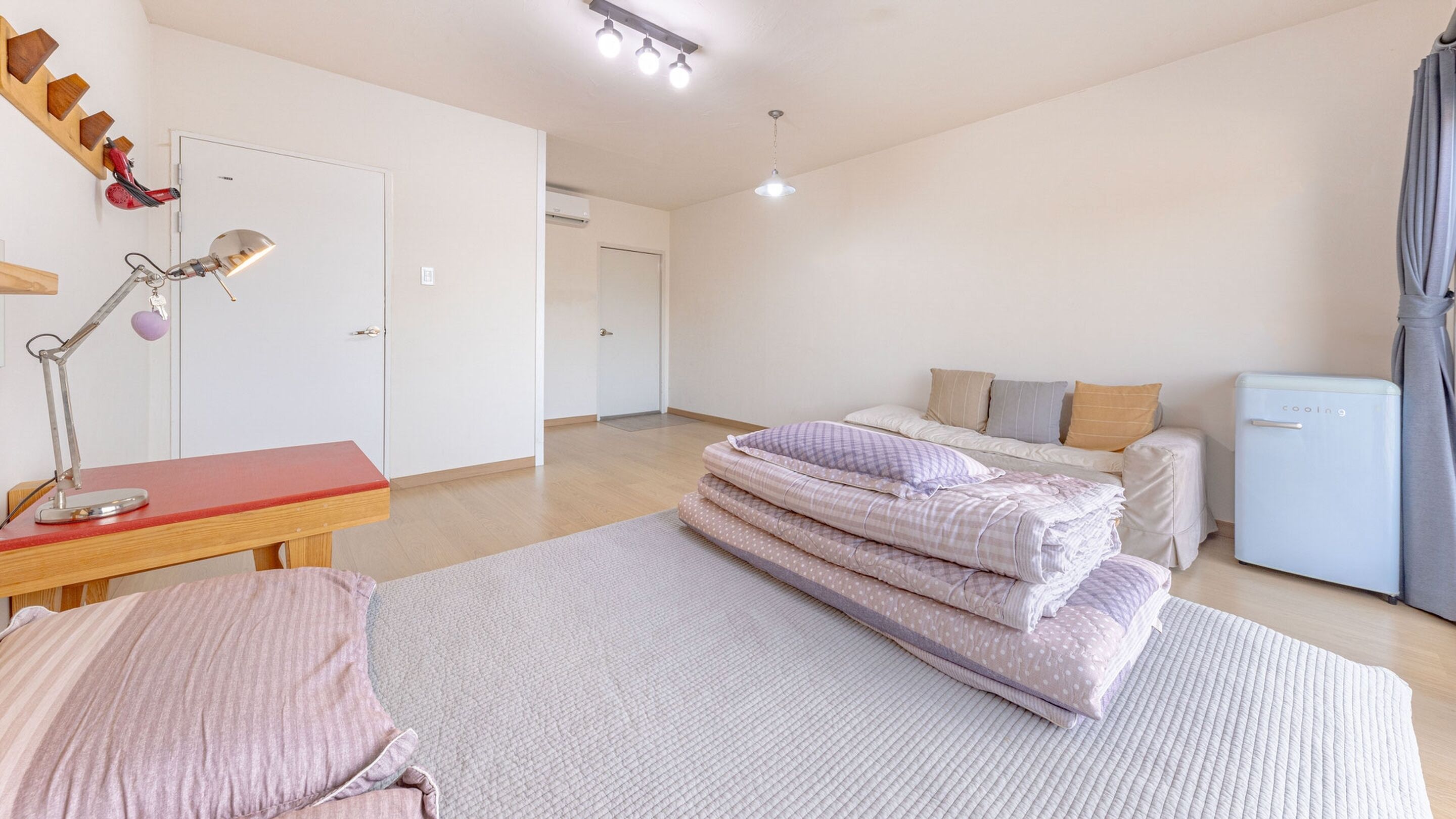 A bedroom with a bed, bedside table, lamp, and a small refrigerator.