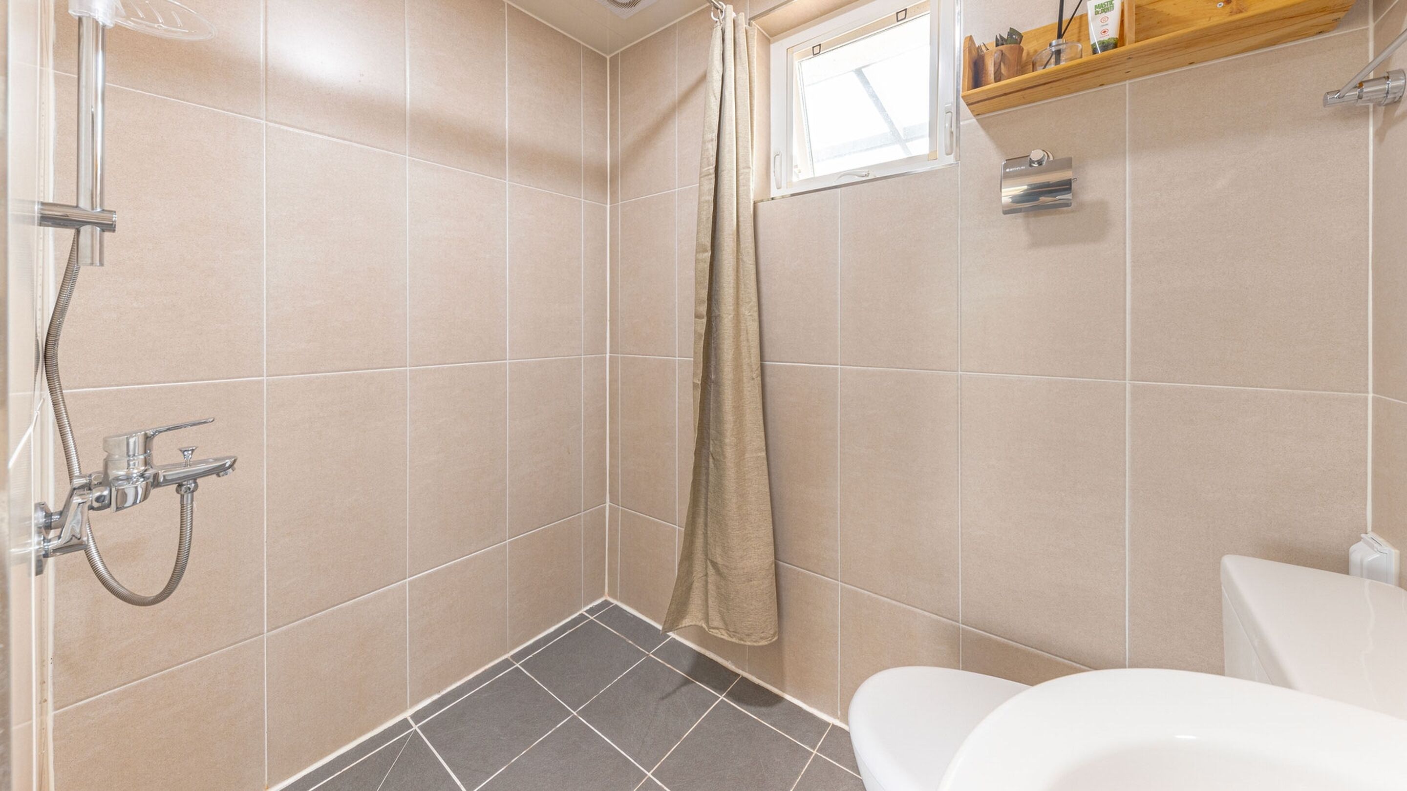 A bathroom with a shower, toilet, and a shelf with toiletries.