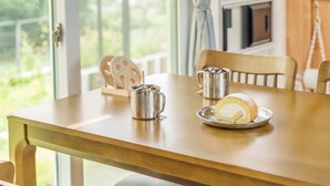A wooden table with a metal mug, a plate with a rolled cake, and a wooden chair. - Ganghwado Labyrinthos Companimal Pension (Incheon)
