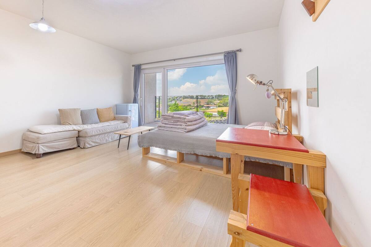 Una habitación moderna y luminosa con una cama, un sofá, un escritorio y un amplio ventanal con vistas al campo.
