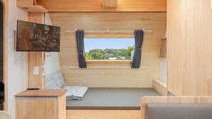 A compact RV interior with a TV, a small seating area, a window with curtains, and a view of greenery. - Ganghwado Labyrinthos Companimal Pension (Incheon)