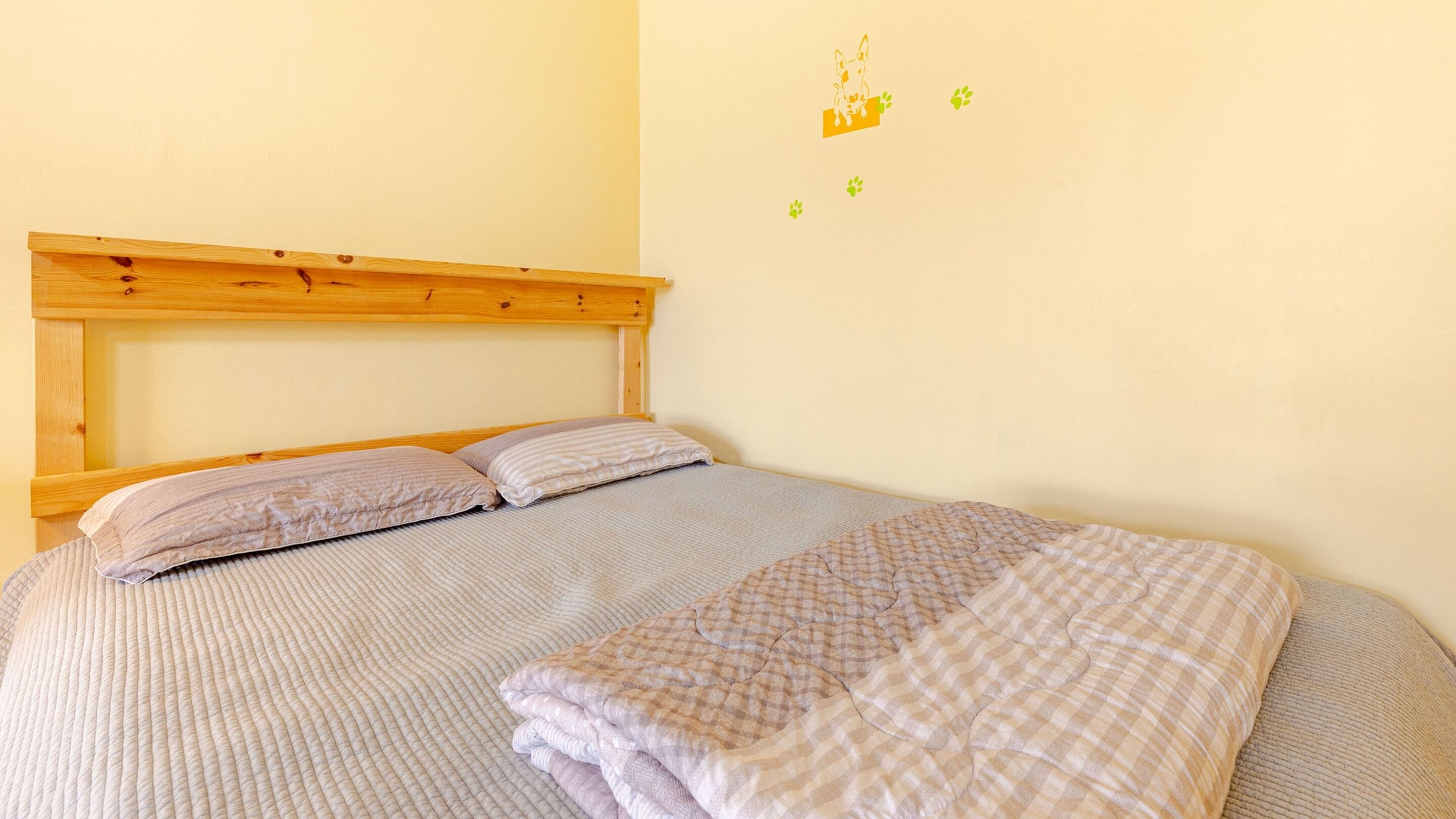 A neatly made bed with a checkered blanket and pillows, a wooden headboard, and a wall with a dog and paw print decoration.