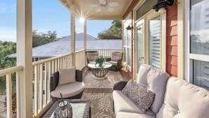 A covered porch with a ceiling fan, a glass-top table with a plant, and a sofa with patterned cushions. - Algun Dia - Plush Family-friendly Home - A Block From Beach (Panama City Beach)