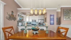 A dining room with a wooden table, blue cushioned chairs, and a decorative bowl centerpiece. - Algun Dia - Plush Family-friendly Home - A Block From Beach (Panama City Beach)