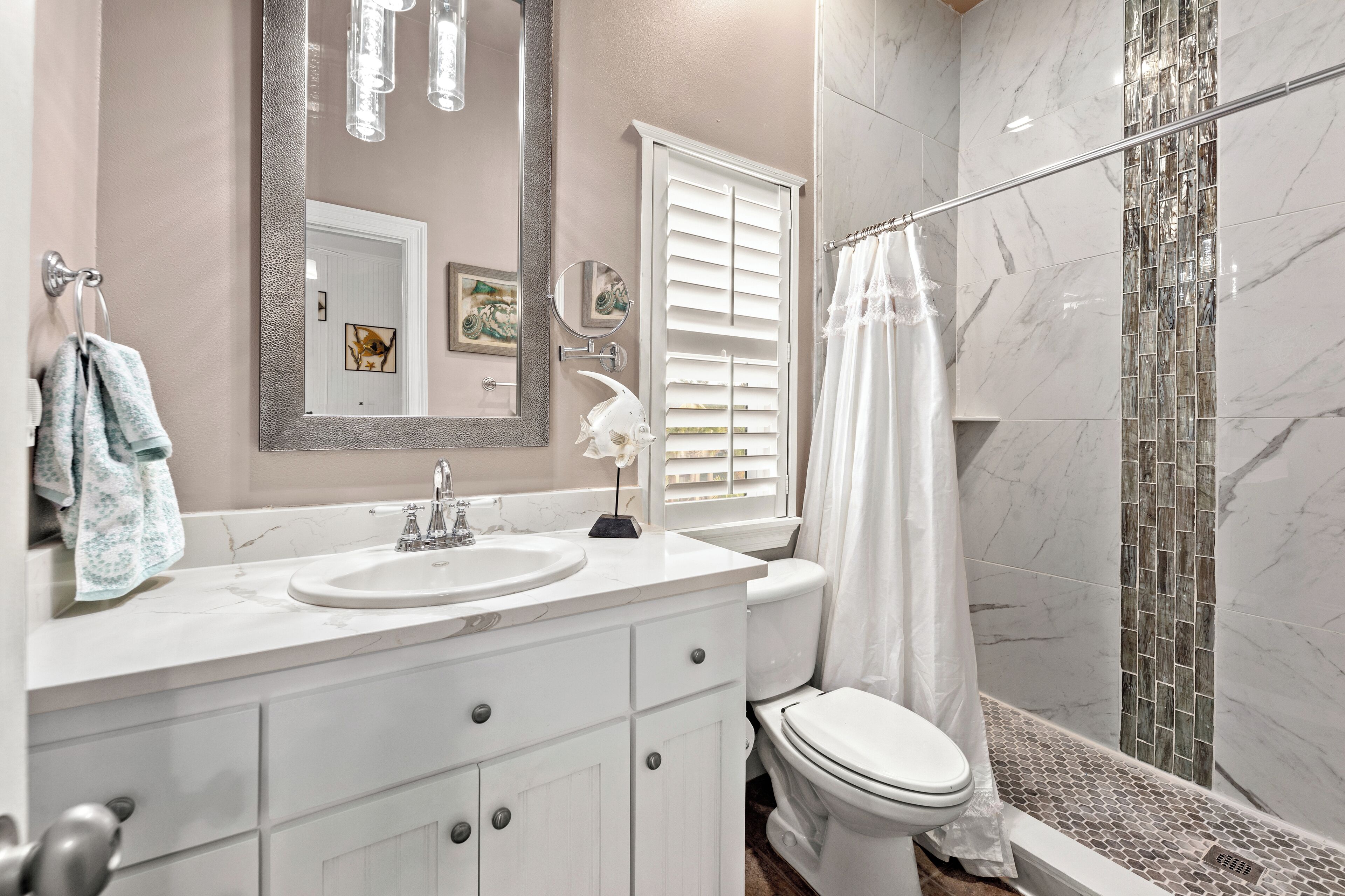 A bathroom with a white vanity, sink, and toilet. There is a shower with a glass door and a tiled shower area.