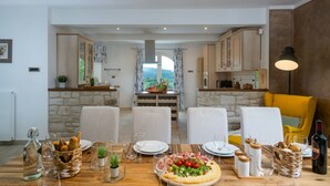 A dining area with a wooden table set for a meal, chairs, and a view of the kitchen in the background. - Villa Casa Brazzana (Buzet)