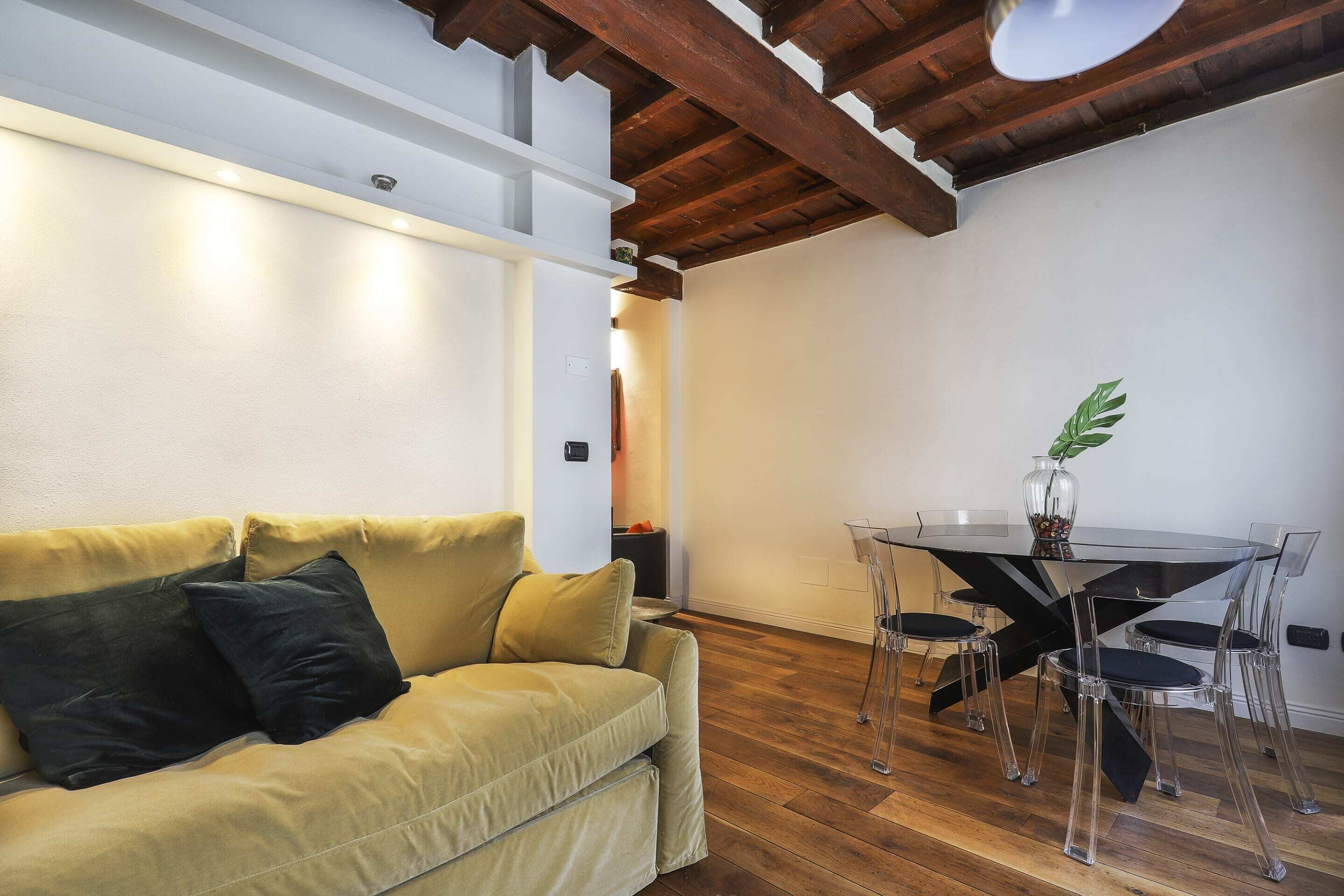 Una habitación con sofá amarillo, una mesa redonda de vidrio y sillas transparentes.